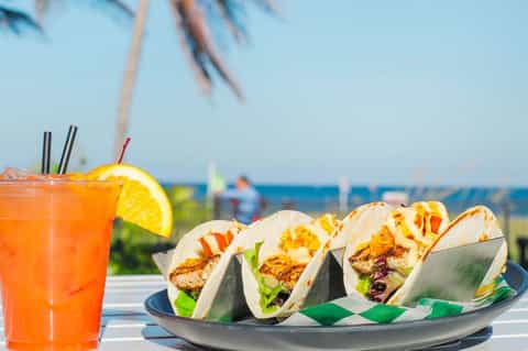 Grilled fish tacos with orange cocktail garnished with citrus slice by beach