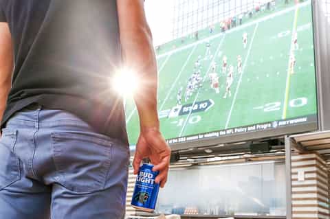Person holding beer watching football game on large screen at sports bar