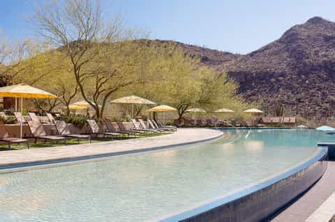 Resort pool with curved edges, loungers under umbrellas, and desert mountain landscape