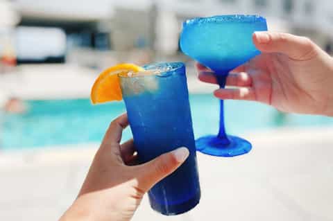 Vibrant blue cocktails by the pool with orange garnish and colorful frozen glasses