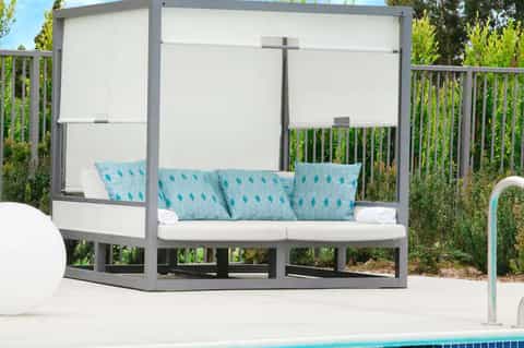 Modern gray canopy bed with white retractable shade and teal patterned pillows on pool deck