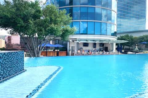 Bright turquoise swimming pool with modern high-rise hotel building and lounge chairs