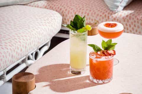 Cocktails with fresh fruit and herbs on a table next to a lounge chair