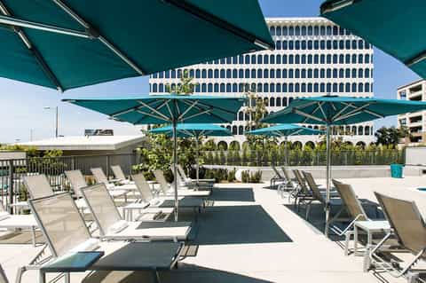 Rooftop lounge with teal umbrellas, white loungers, and modern high-rise building backdrop