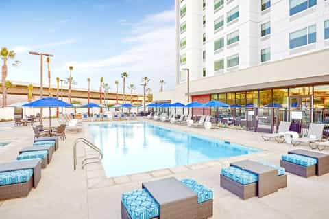 Resort pool with blue umbrellas, palm trees, modern white building, and lounge chairs