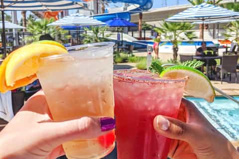 Colorful tropical cocktails with citrus garnish by poolside with umbrellas and water features in background
