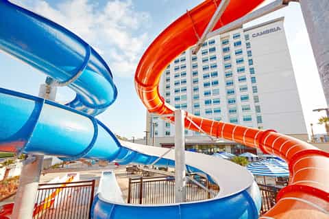 Blue and red water slides at resort with Cambria hotel building in background