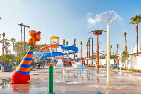 Colorful water park with splash pads, slides, and fountains surrounded by palm trees