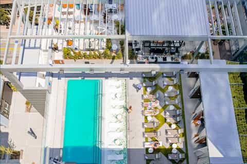 Aerial view of modern rooftop pool with turquoise water, lounge chairs, and surrounding decks