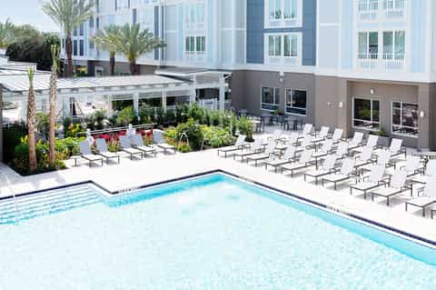 Resort swimming pool with lounge chairs, palm trees, and modern brick building