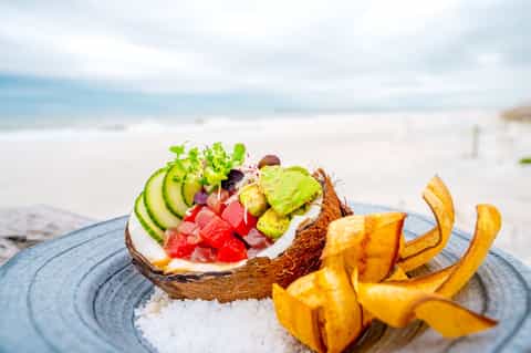 Healthy beach meal: avocado toast with vegetables and plantain chips on blue plate by ocean