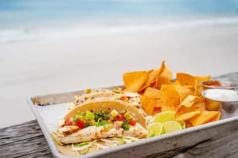 Grilled fish tacos with crispy chips and lime on white plate served beachside