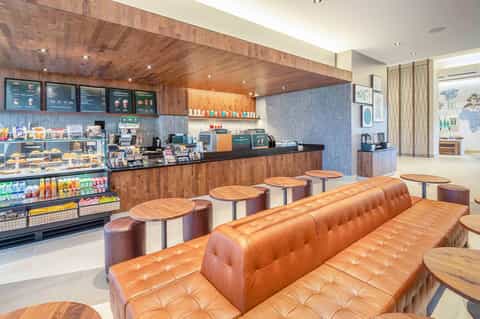 Modern hotel café with orange leather seating, wood ceiling, menu boards, and beverage display cases