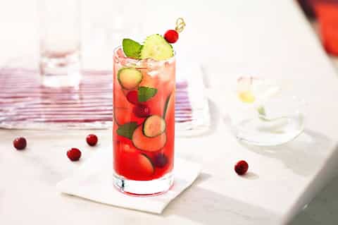 Colorful cocktail with red berries, lime, and mint garnish on white coaster at outdoor dining table