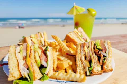 Beach lunch plate with sandwiches and fries, tropical drink with umbrella, ocean view
