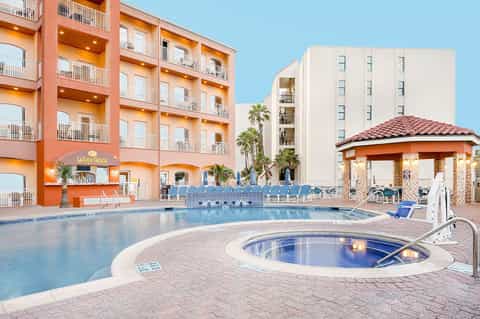 Orange and cream resort buildings with swimming pool and hot tub surrounded by palm trees