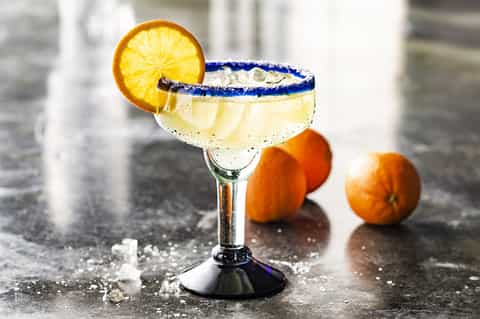 Margarita cocktail with blue salt rim and orange slice garnish, surrounded by fresh oranges