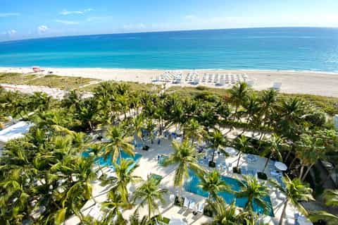 Beachfront resort with pools, palm trees, and white umbrellas overlooking turquoise ocean