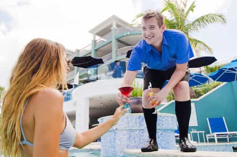 Server in blue shirt delivering cocktail to woman at poolside bar with ocean view
