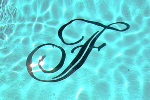 Elegant cursive 'F' logo reflected in clear turquoise pool water