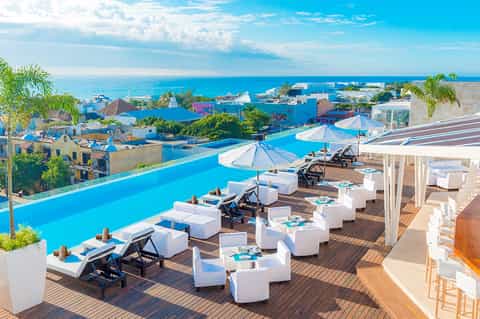 Rooftop infinity pool overlooking coastal town with ocean view and white umbrellas