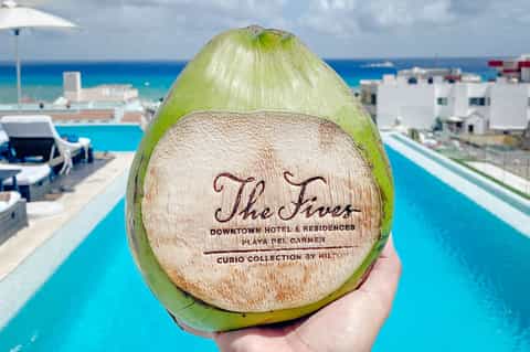 Coconut with carved hotel branding held up against turquoise pool and coastal resort backdrop
