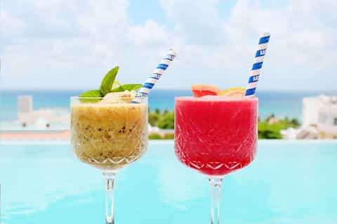 Two tropical cocktails with striped straws overlooking an ocean and coastline