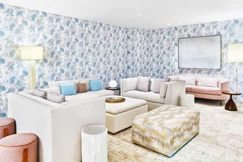Elegant lounge with blue botanical wallpaper, cream seating arrangements, and decorative poufs with neutral tones