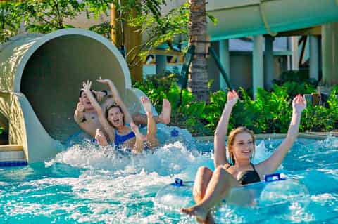 Children enjoying a water slide at a resort pool with tropical landscaping and lounge chairs