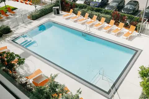 Aerial view of rectangular pool with orange lounge chairs and white umbrellas on concrete deck
