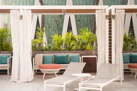Outdoor resort patio with white cabanas, lounge chairs, and tropical plants
