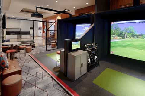 Indoor golf simulator lounge with bronze accents, comfortable seating, and large projection screens