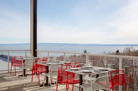 Waterfront dining terrace with red chairs overlooking calm bay waters