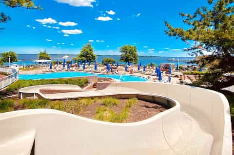Waterfront pool complex with water slides, blue umbrellas, and scenic lake view