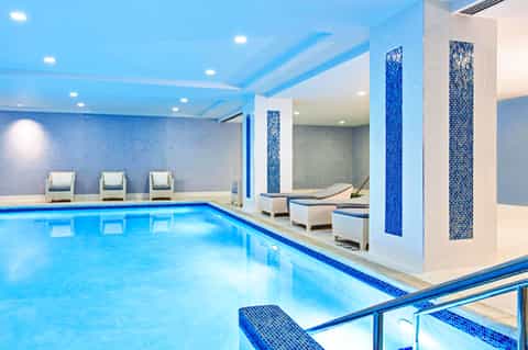 Indoor lap pool with blue mosaic tile accents, lounge chairs, and modern spa facilities