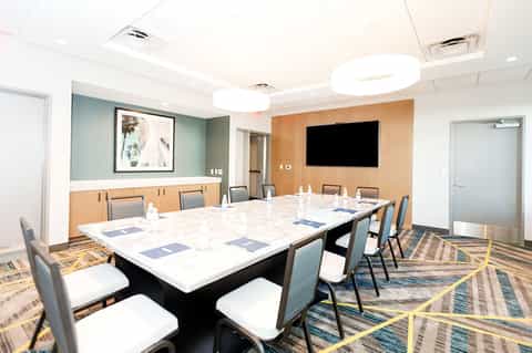 Professional conference room with long white table, blue chairs, and presentation screen