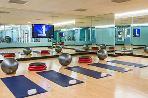 Fitness studio with yoga mats, exercise balls, and mirrors with TV screens for classes