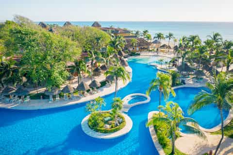 Aerial view of sprawling resort with curved blue pools, palm trees, and beachfront access