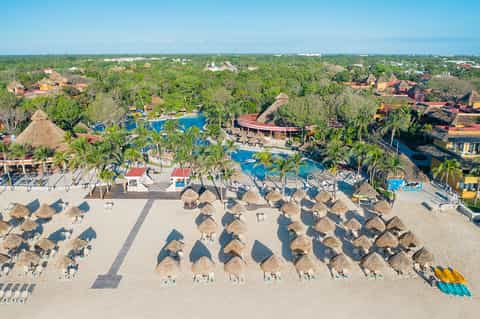 Aerial view of all-inclusive resort beach with thatched umbrellas, pools, and lush grounds