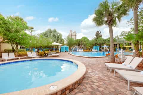 Resort pool area with loungers, palm trees, and multi-level swimming pools under blue sky