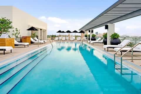Rooftop lap pool with lounge chairs, black umbrellas, and city skyline views