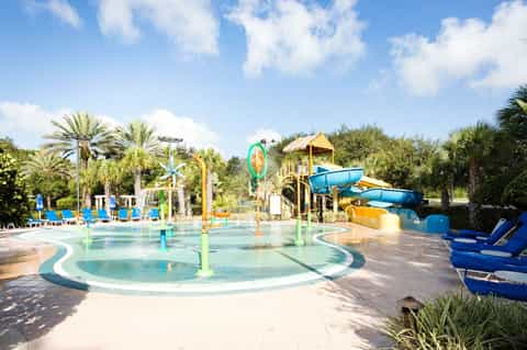 Colorful water park with splash pad, slides, palm trees, and tiki-style structures