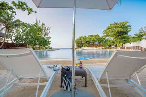 Beach loungers under umbrella with snorkeling gear and drinks overlooking calm lagoon