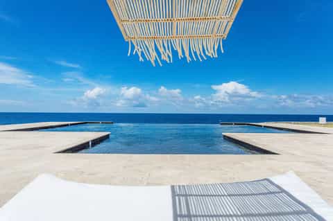Oceanfront infinity pool with woven shade structure and turquoise water meeting horizon