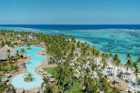 Aerial view of tropical beach resort with curved pool, palm trees, and turquoise ocean