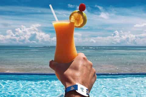 Hand holding tropical cocktail with orange slice and cherry over ocean view