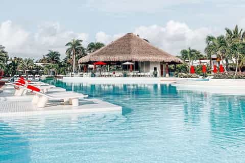 Lagoon-style pool with white loungers, tiki bar, and palm trees