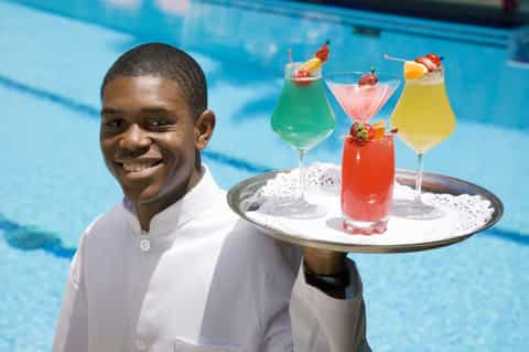 Server in white shirt holding tray of colorful cocktails by bright blue pool