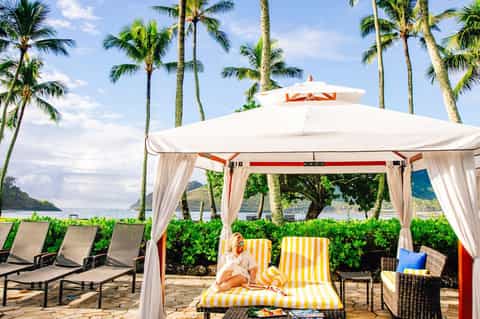 Beach cabana with white canopy and yellow striped loungers under tall palm trees with ocean view