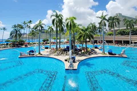 Resort pool complex with palm trees and ocean view in background